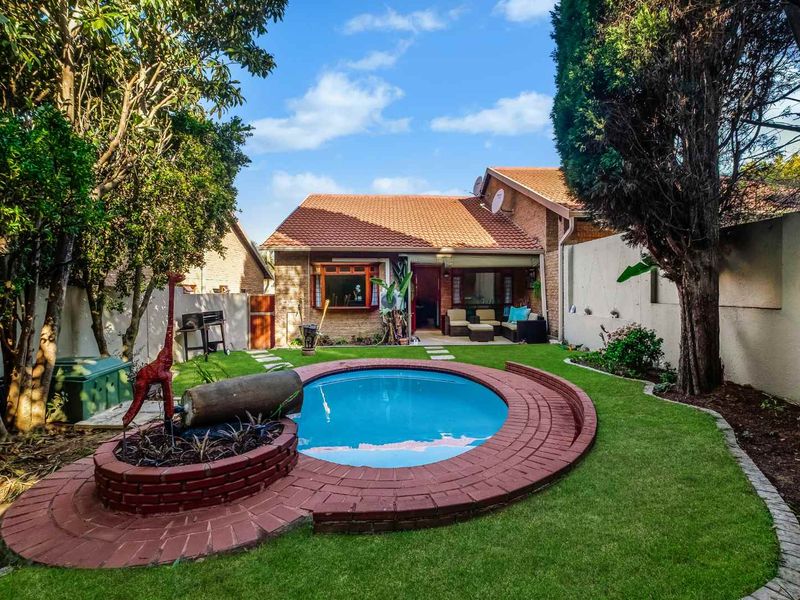 Rear garden view featuring a circular swimming pool with brick surround, landscaped lawn, and established trees against the brick house facade.