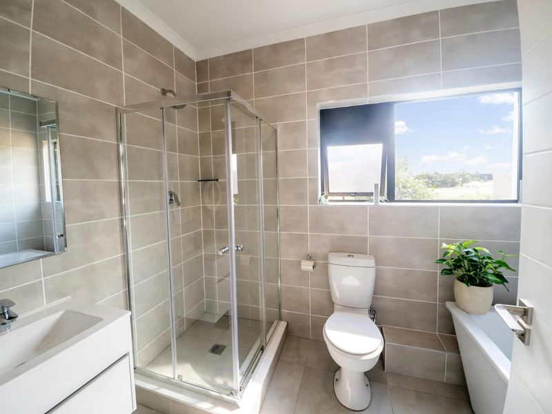 Modern bathroom featuring a glass shower enclosure, wall-mounted vanity, ceramic toilet, and a built-in bathtub with neutral floor-to-ceiling tiling.
