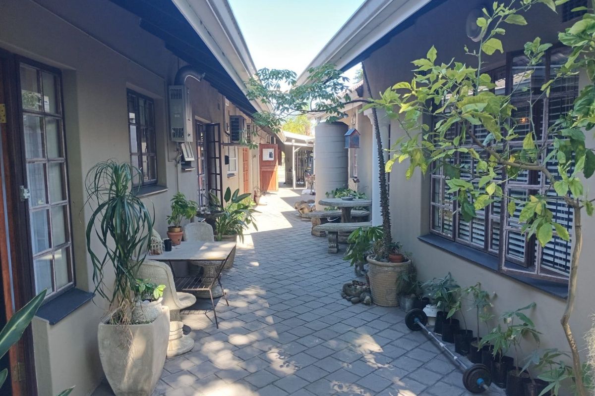 A paved outdoor walkway between two building wings, featuring fixed gas geyser infrastructure, water storage tank, and classic timber-framed windows.