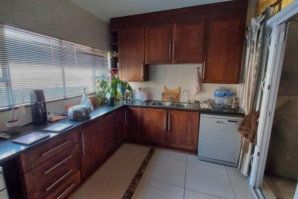 A functional kitchen featuring dark wood cabinetry, granite countertops, a double basin sink, and tiled flooring with large windows for natural light.