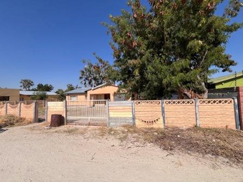 Front view of a residential property featuring a precast concrete boundary wall, metal gates, and a corrugated metal roof structure.