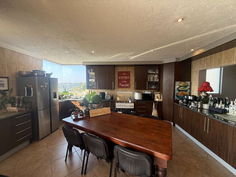 Spacious kitchen featuring dark wood cabinetry, granite countertops, tiled backsplash, and a large window with scenic views, integrated with a dining area.