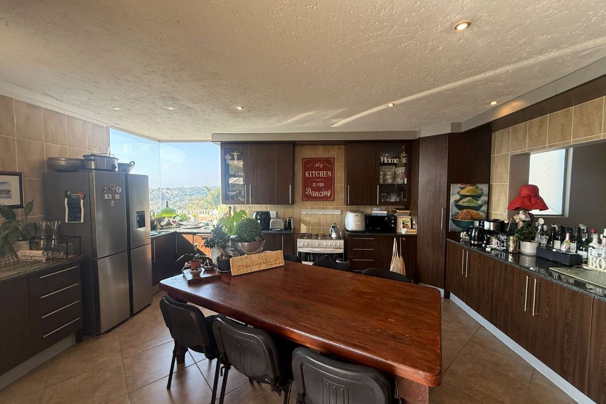 Spacious kitchen featuring dark wood cabinetry, granite countertops, tiled backsplash, and a large window with scenic views, integrated with a dining area.