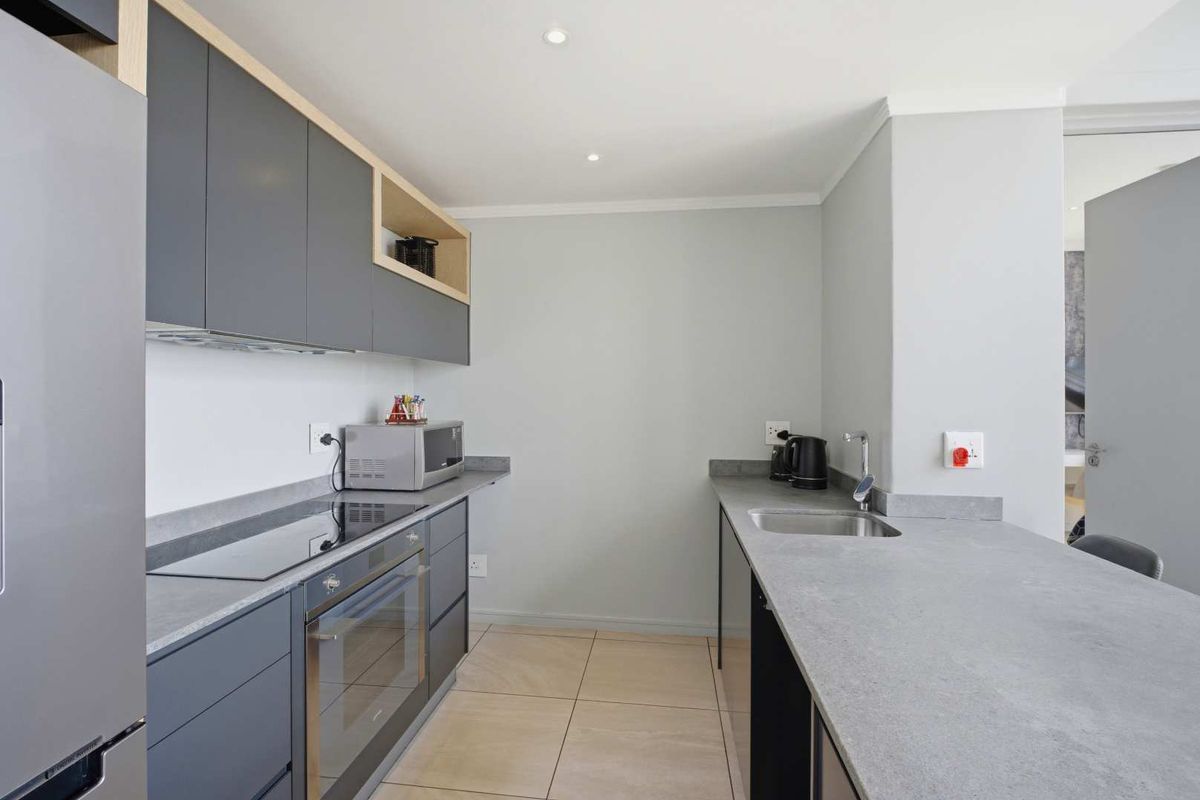 Modern galley-style kitchen featuring sleek grey cabinetry, stone-look countertops, integrated oven, and induction hob with recessed ceiling lighting.