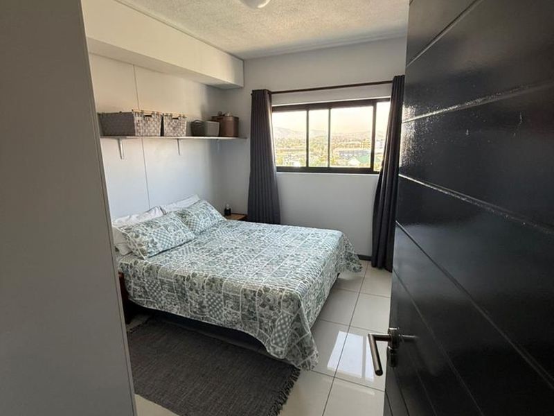 A well-lit bedroom featuring tiled flooring, built-in wall shelving, and a window offering an elevated view.