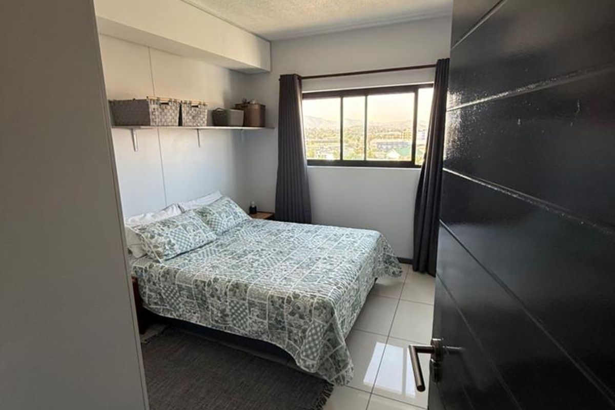 A well-lit bedroom featuring tiled flooring, built-in wall shelving, and a window offering an elevated view.