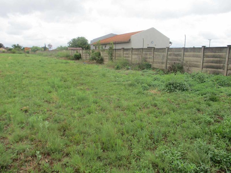 A vacant residential plot featuring overgrown grass and a precast concrete boundary wall with installed electric fencing.