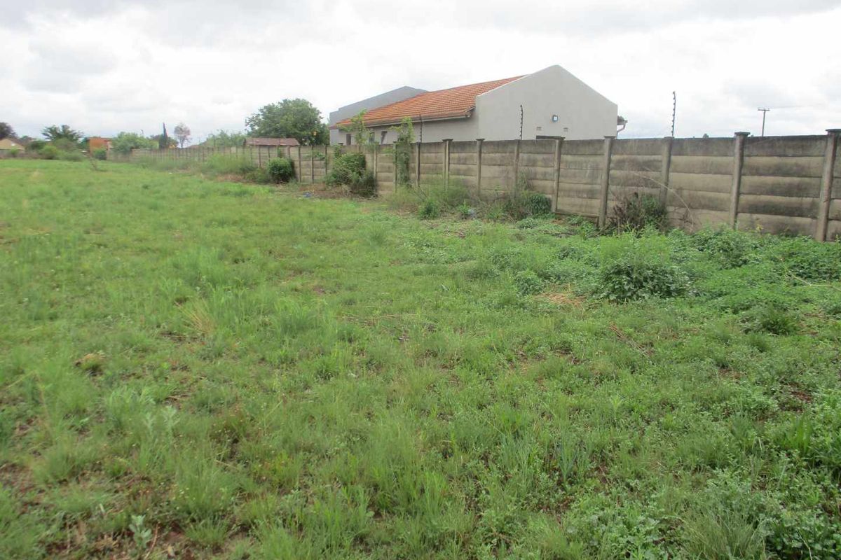 A vacant residential plot featuring overgrown grass and a precast concrete boundary wall with installed electric fencing.