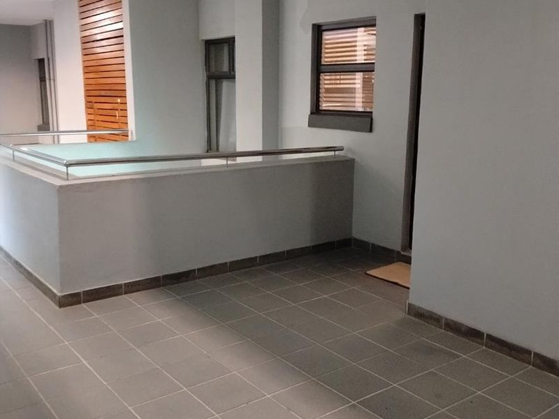 A clean, modern balcony area featuring tiled flooring, a stainless steel balustrade, and a decorative timber slat feature wall.