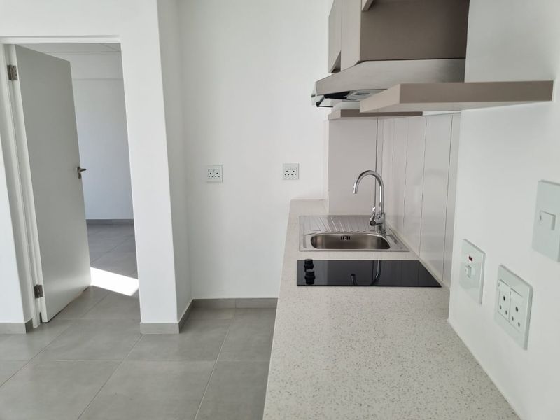 A modern, compact kitchen featuring stone countertops, a stainless steel sink, an electric hob, and an extractor fan, finished with neutral tiling.