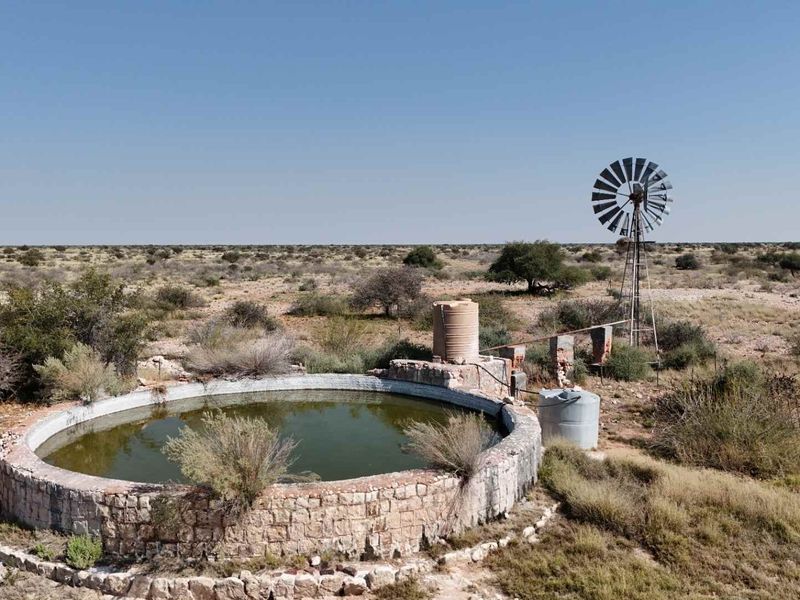 Aerial view of a farm water reservoir featuring a traditional windmill, stone masonry construction, and water storage tanks in a rural landscape.