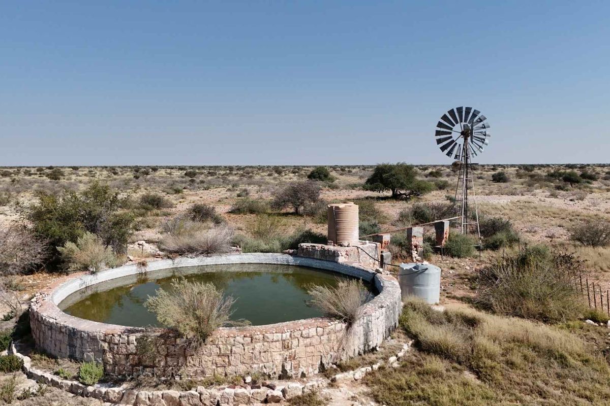 Aerial view of a farm water reservoir featuring a traditional windmill, stone masonry construction, and water storage tanks in a rural landscape.