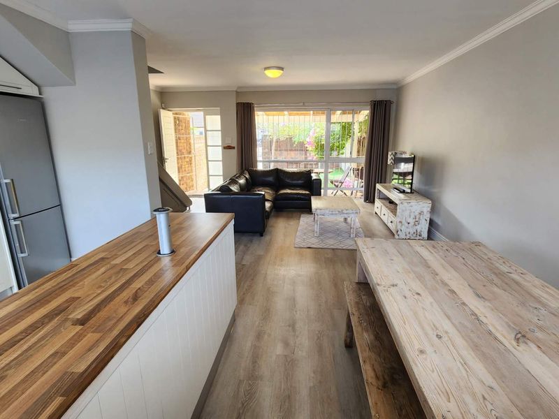 Open-plan living area featuring a kitchen with wooden countertops, laminate flooring, and a sliding glass door leading to the rear outdoor space.