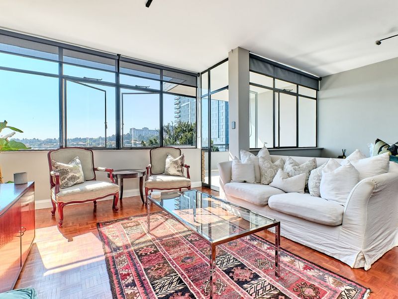 Bright and spacious living area featuring classic parquet flooring, expansive aluminium-framed windows offering natural light, and modern track lighting.