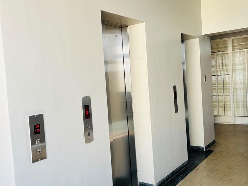 A communal apartment hallway featuring two stainless steel elevators and tiled flooring leading to a glass-paneled entrance door.