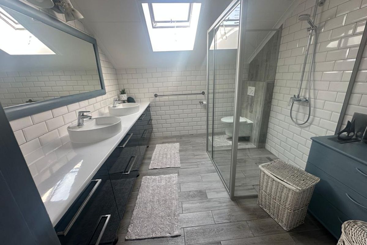 Modern bathroom featuring a double vanity with vessel sinks, a glass-enclosed walk-in shower, subway tile wall finishes, and a skylight for natural illumination.