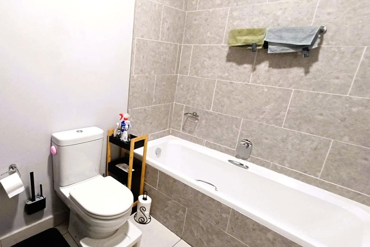 A functional bathroom featuring a built-in bathtub with tiled surround, a standard toilet, and wall-mounted towel rails.