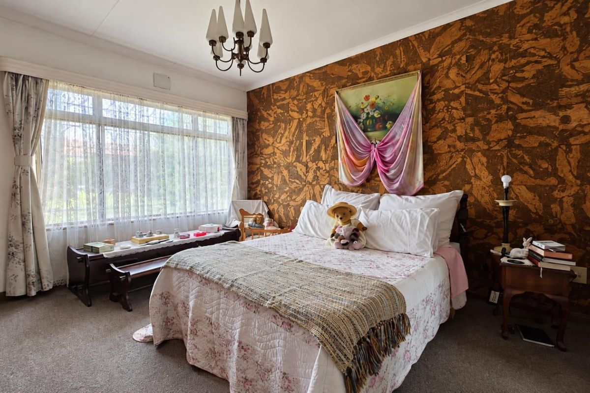 A bedroom featuring a large window for natural light and a distinctive textured feature wall, offering a dated aesthetic ready for modernization.