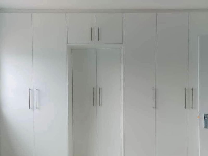 A bedroom featuring floor-to-ceiling white built-in cupboards with modern handles, providing ample storage space.