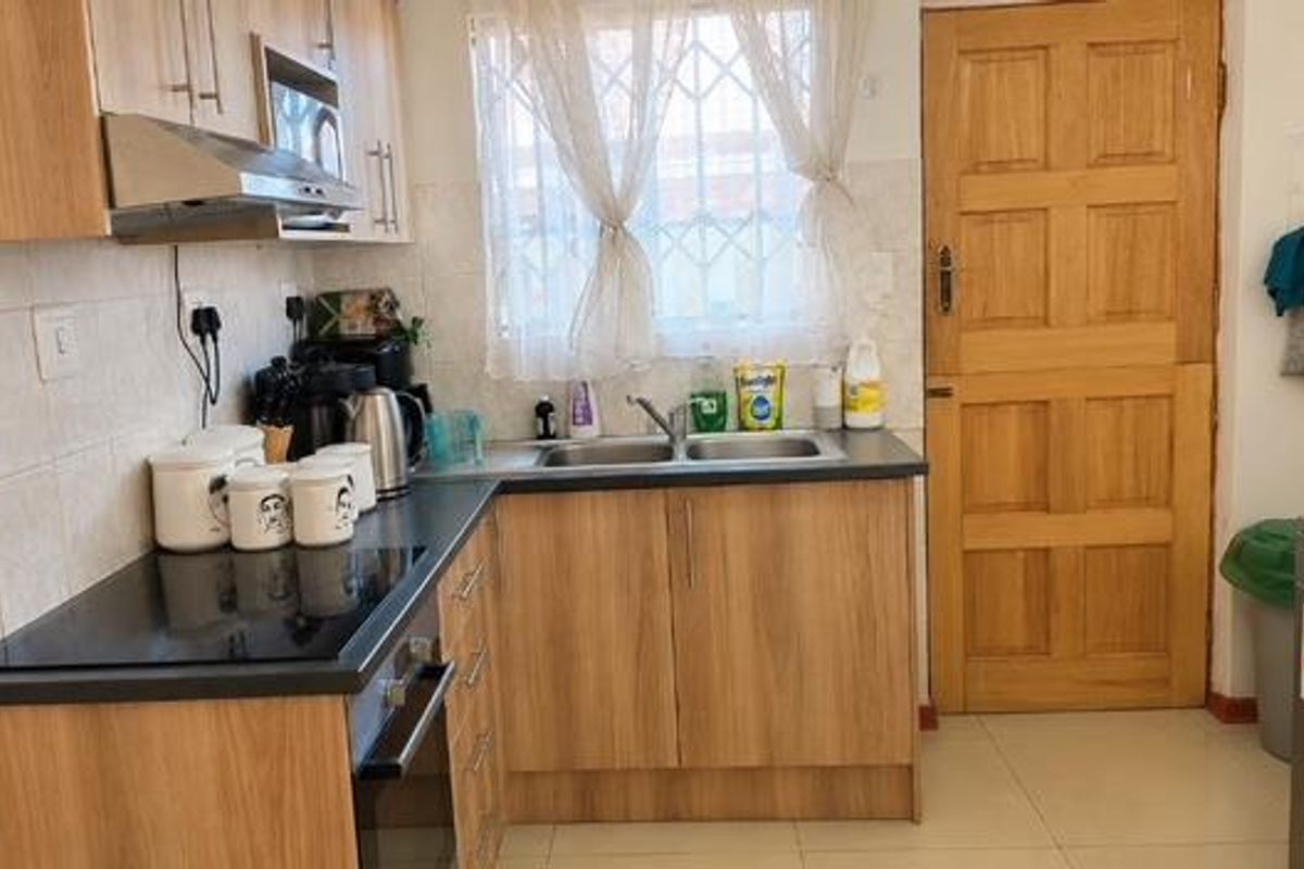 A functional kitchen featuring light wood-look cabinetry, a built-in oven with hob, extractor fan, and a stainless steel double sink with tiled splashback.