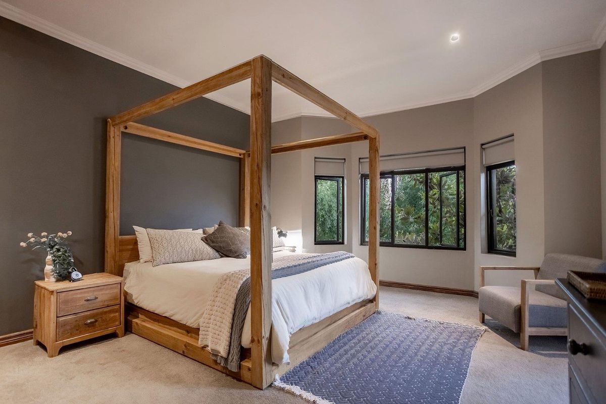 A spacious bedroom featuring neutral walls, carpeted flooring, and large windows that provide natural light and garden views.