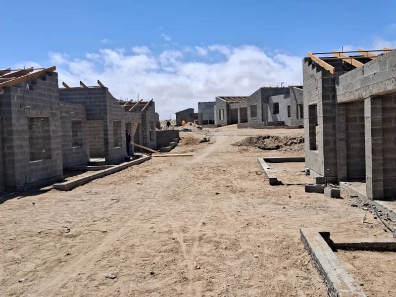 A construction site showing multiple townhouse units in the early stages of development with exposed concrete block walls and timber roof trusses.