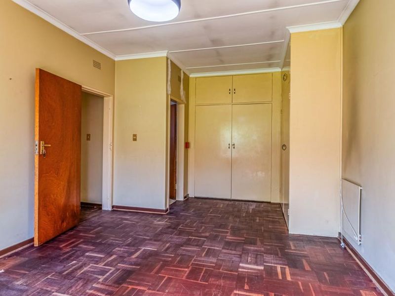 An empty bedroom featuring original parquet flooring, built-in cupboards, and neutral wall finishes, offering a blank canvas for renovation.