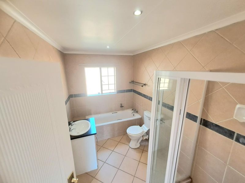 A functional bathroom featuring a built-in bathtub, separate shower enclosure, toilet, and a vanity basin with neutral wall and floor tiling.