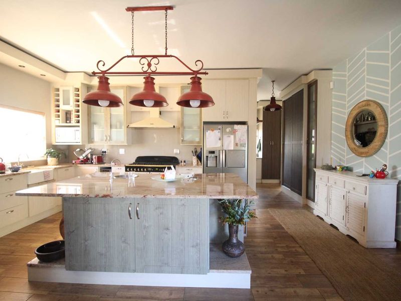 Spacious kitchen featuring a large central island with granite countertops, farmhouse sink, gas cooktop, and ample built-in cabinetry with hardwood flooring throughout.