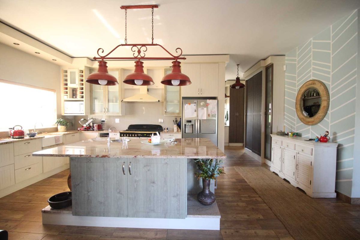 Spacious kitchen featuring a large central island with granite countertops, farmhouse sink, gas cooktop, and ample built-in cabinetry with hardwood flooring throughout.