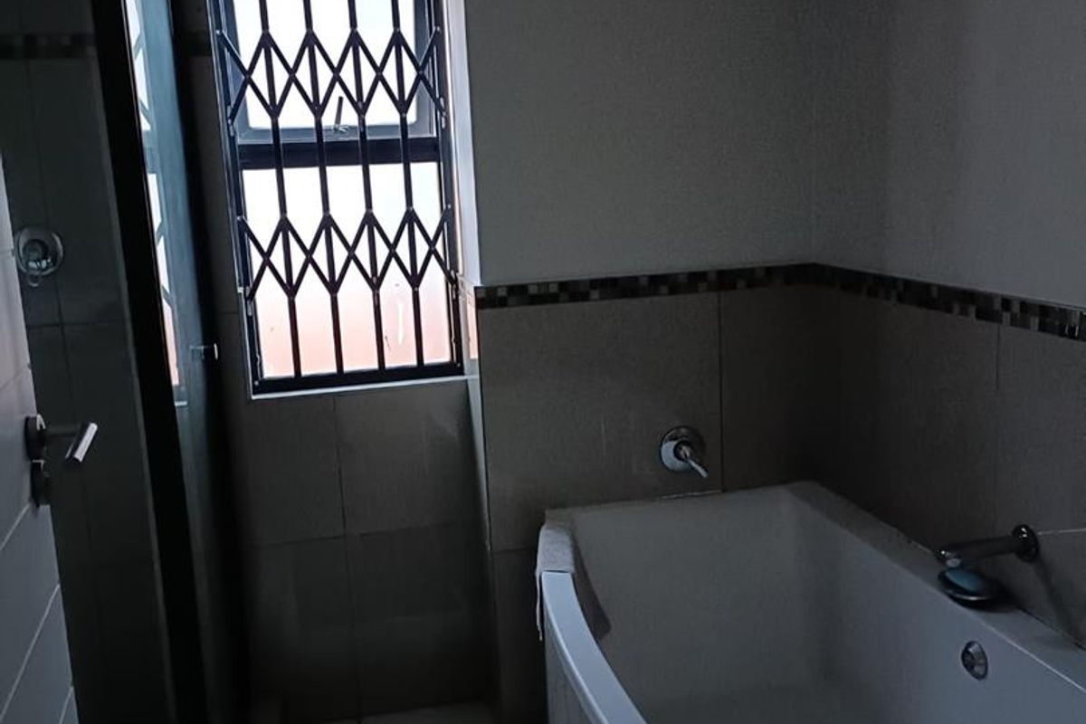 A functional bathroom featuring a built-in bathtub, a separate shower enclosure, and a window with security bars.