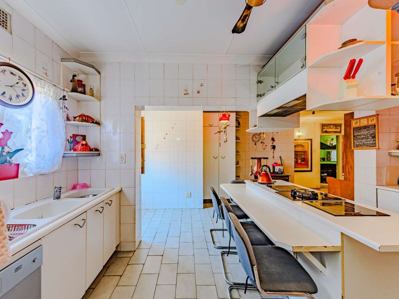 A dated kitchen featuring built-in cabinetry, a breakfast bar, integrated hob, and tiled finishes, offering significant potential for a modern renovation.