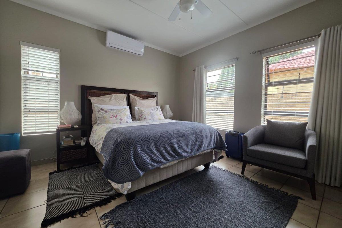 A well-lit bedroom featuring tiled flooring, a wall-mounted air conditioning unit, and a ceiling fan, providing a comfortable and functional living space.