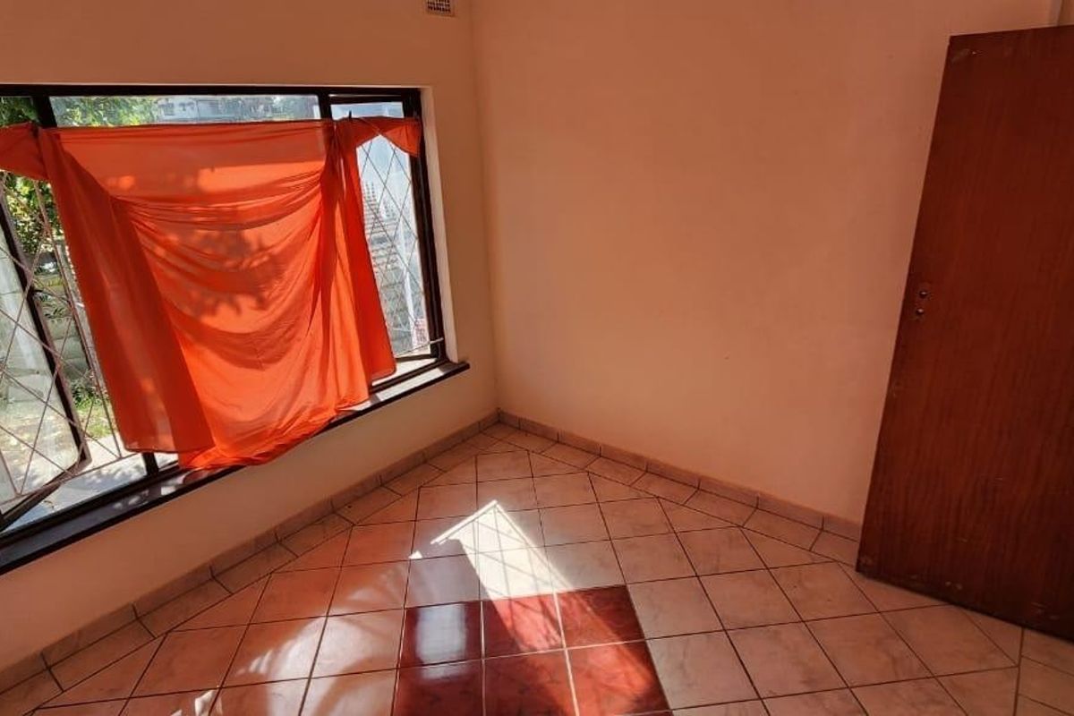 An empty bedroom featuring tiled flooring, a timber door, and a window fitted with security bars.