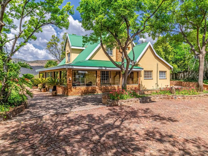A charming farmhouse exterior featuring a green metal roof, brick facade, and an enclosed patio area surrounded by mature trees and stone landscaping.