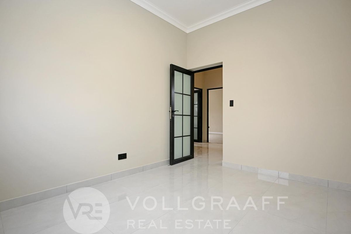 A bright, empty room featuring neutral wall tones, polished tile flooring, and a modern black-framed glass door leading to an adjacent space.