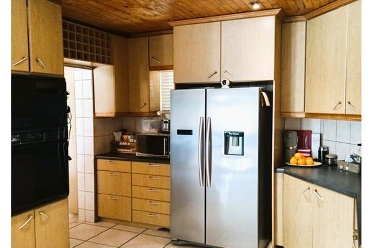 Functional kitchen featuring light wood cabinetry, dark countertops, tiled flooring, and a timber-paneled ceiling with integrated downlights.