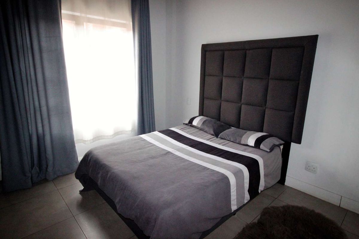 A well-maintained bedroom featuring neutral tiled flooring and a large window with curtains, providing a clean and functional living space.