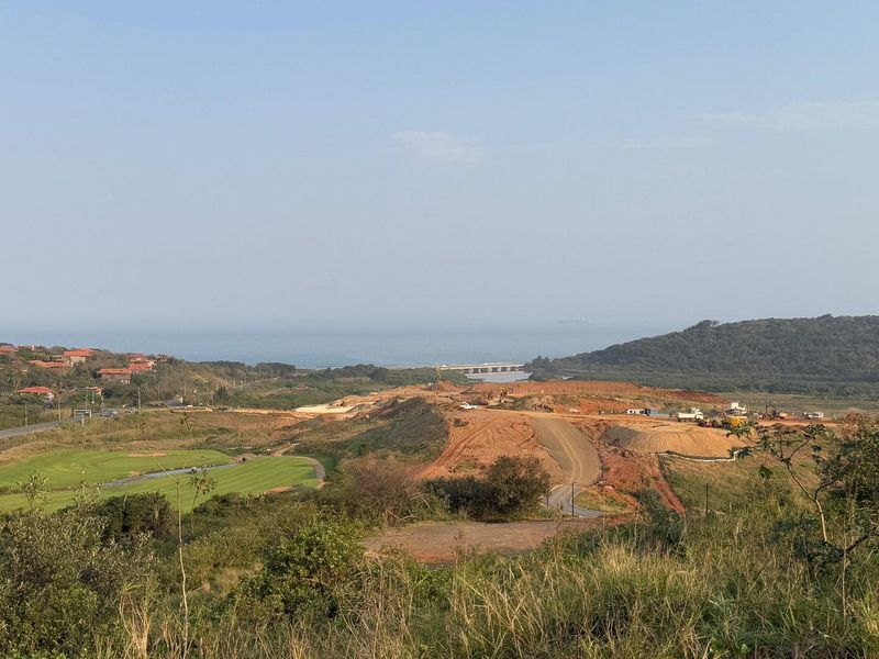 A wide-angle view of the surrounding landscape, featuring coastal scenery, a golf course, and ongoing road development in the distance.