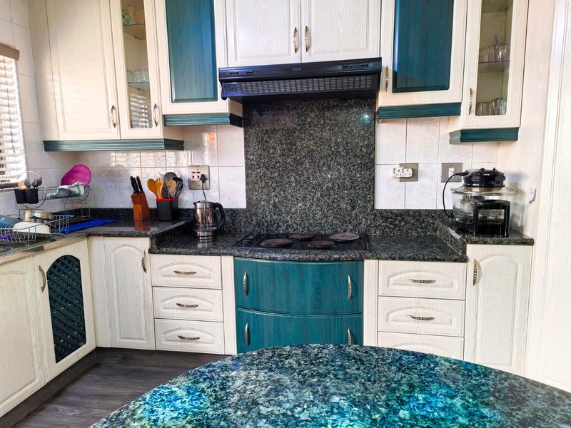A functional kitchen featuring granite countertops, a built-in electric hob with extractor fan, and two-tone cabinetry with ample storage space.