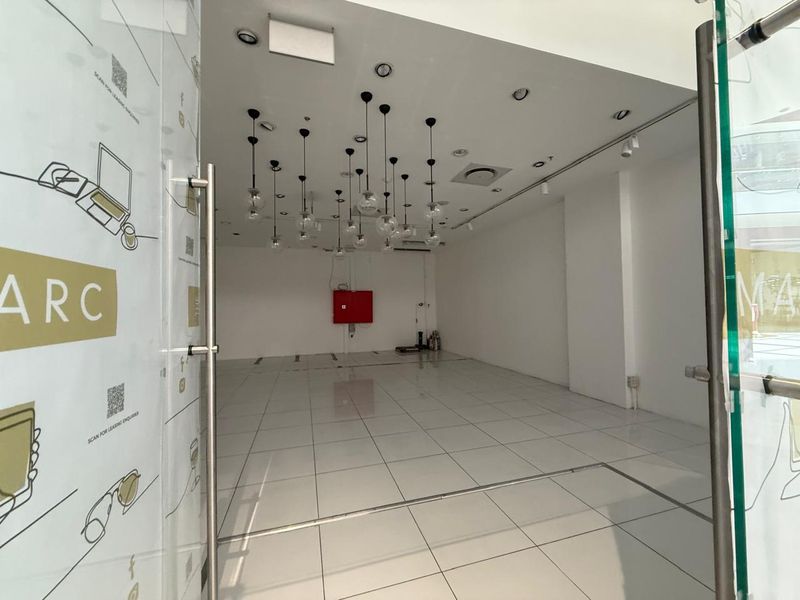 A bright, empty retail unit featuring polished tiled flooring, modern pendant lighting, and a glass entrance door, suitable for a variety of commercial uses.