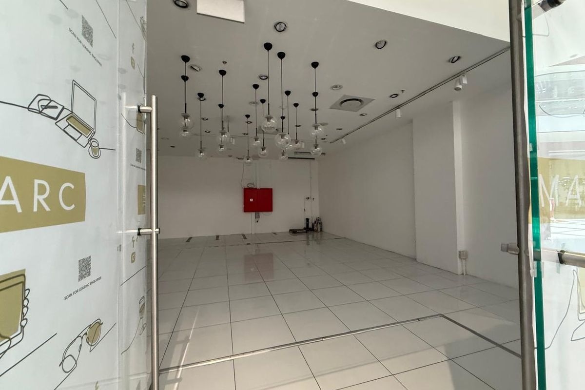 A bright, empty retail unit featuring polished tiled flooring, modern pendant lighting, and a glass entrance door, suitable for a variety of commercial uses.
