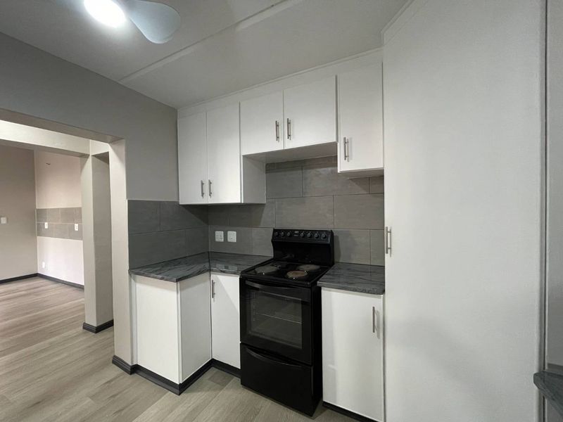 A clean, modern kitchen featuring white cabinetry, grey tiled backsplash, laminate countertops, and a freestanding stove, with neutral laminate flooring throughout.