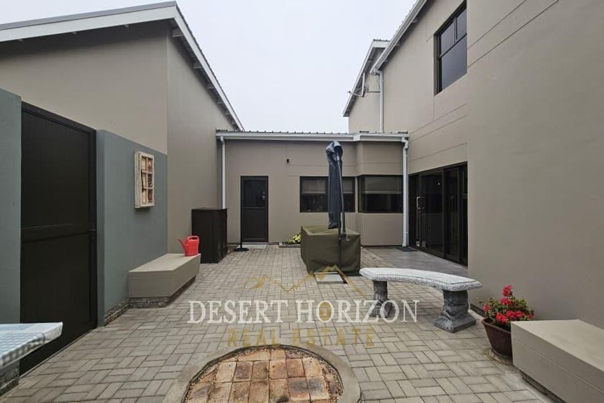 A paved rear courtyard area featuring a built-in fire pit, integrated bench seating, and direct access to the main dwelling.