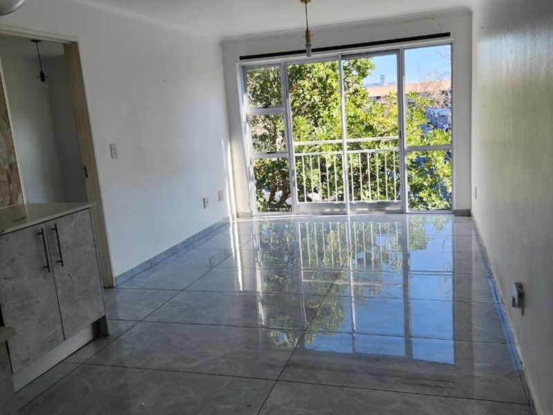 Bright open-plan living area featuring modern large-format grey floor tiles and a large sliding glass door leading to a balcony.