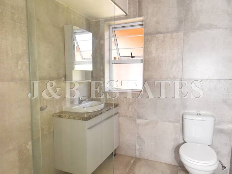 Modern bathroom featuring a glass-enclosed shower, vanity with basin, and toilet, finished with neutral floor-to-ceiling wall tiles.