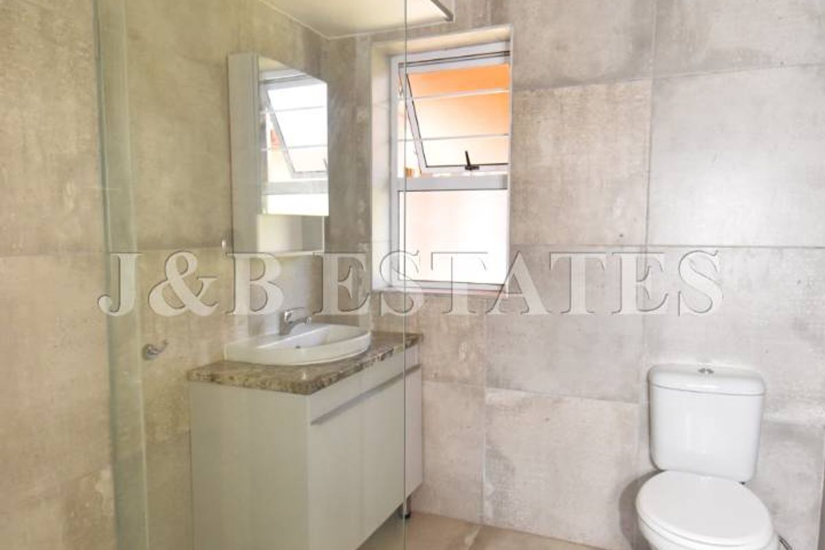 Modern bathroom featuring a glass-enclosed shower, vanity with basin, and toilet, finished with neutral floor-to-ceiling wall tiles.