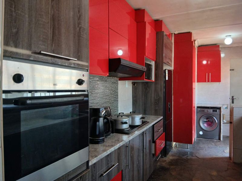 Modern kitchen featuring high-gloss red cabinetry, wood-grain base units, stone countertops, built-in oven, and integrated laundry space with tiled flooring.