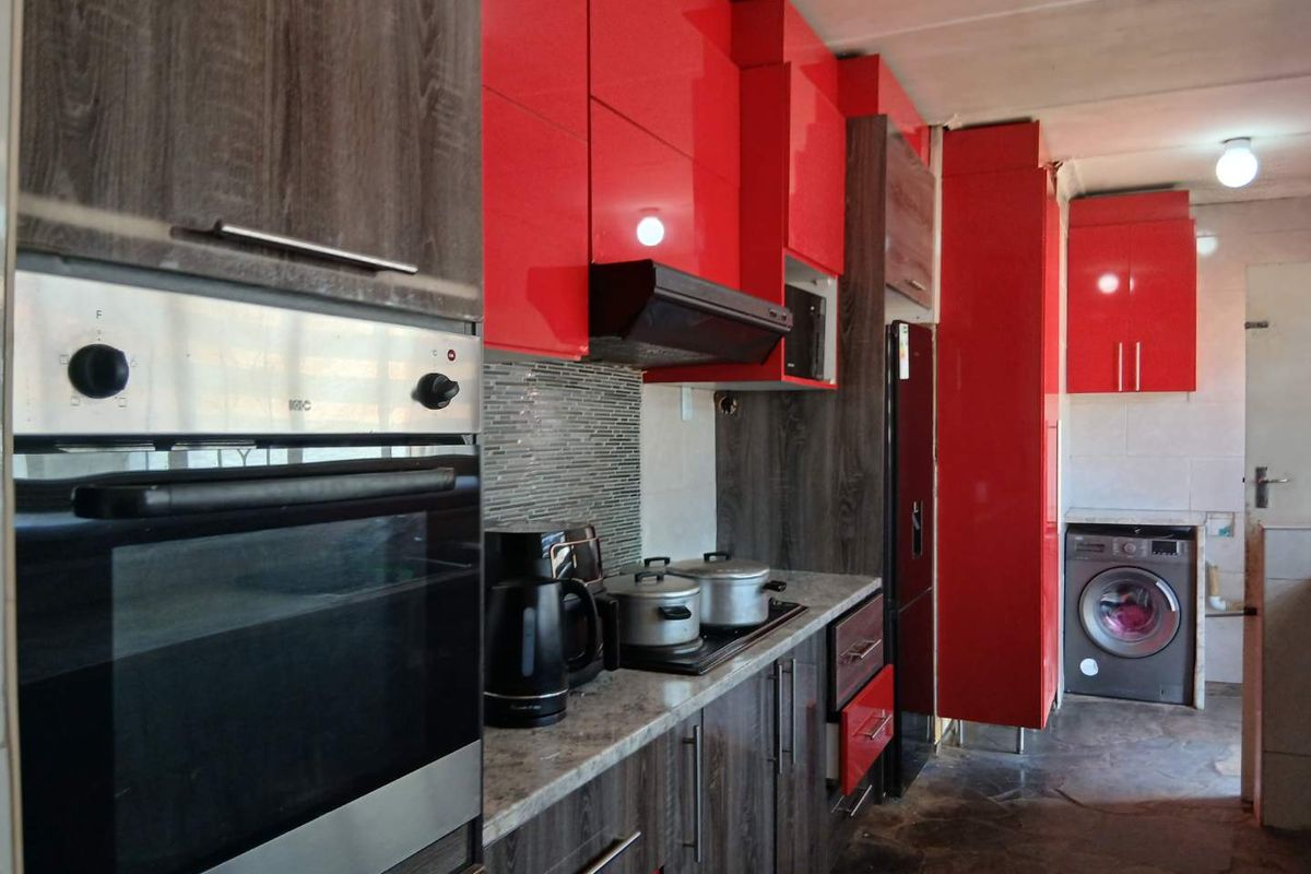 Modern kitchen featuring high-gloss red cabinetry, wood-grain base units, stone countertops, built-in oven, and integrated laundry space with tiled flooring.