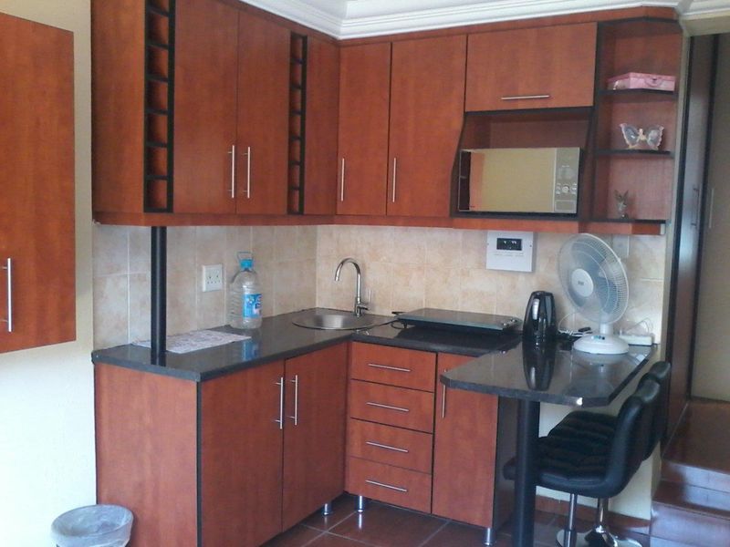 Compact kitchen featuring wood-finish cabinetry, granite countertops, a built-in microwave, and a small breakfast bar area with tiled backsplash.